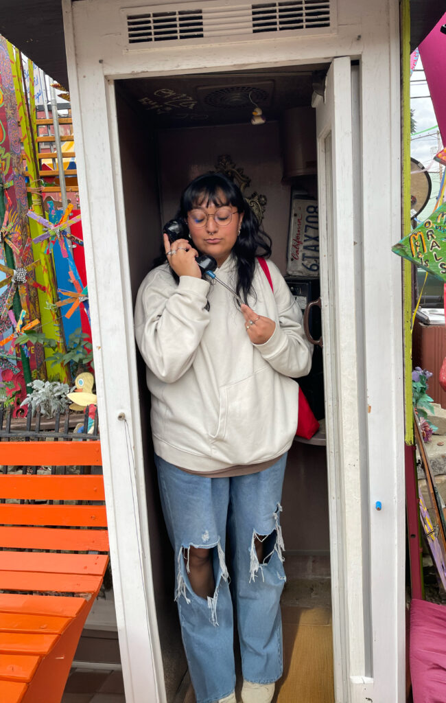 a woman standing in a colorful phone booth, holding the phone.