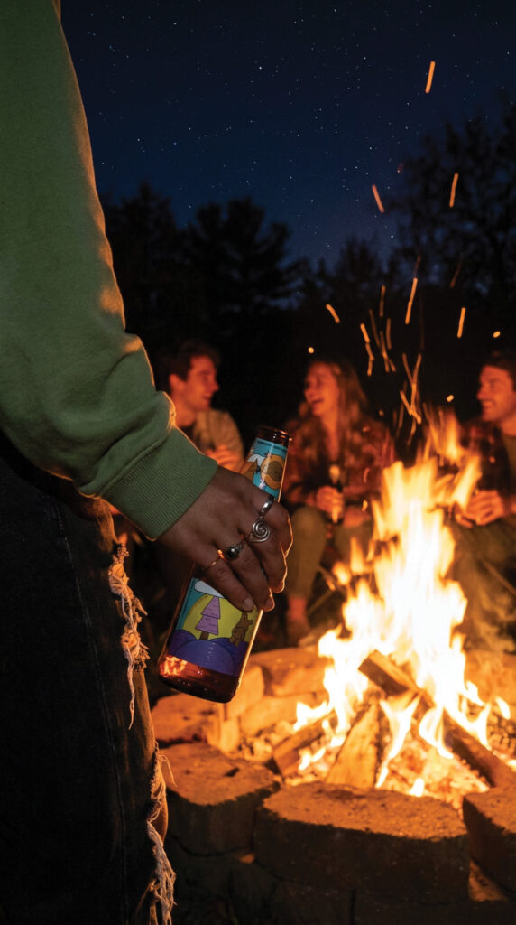 Someone holding a lagunitas bottle while standing by a bonfire.